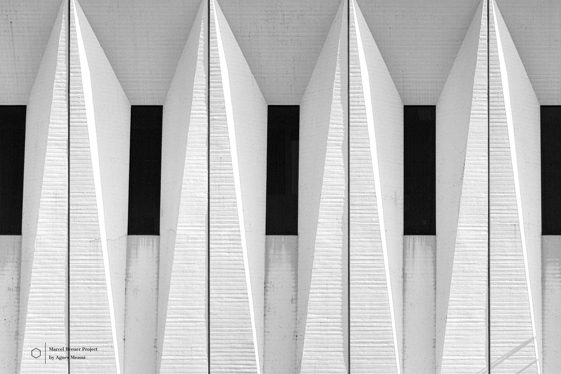 Close-up of the iconic repetitive triangular concrete facade elements of the Mundipharma headquarters, creating a sharp rhythmic pattern of light and shadow.