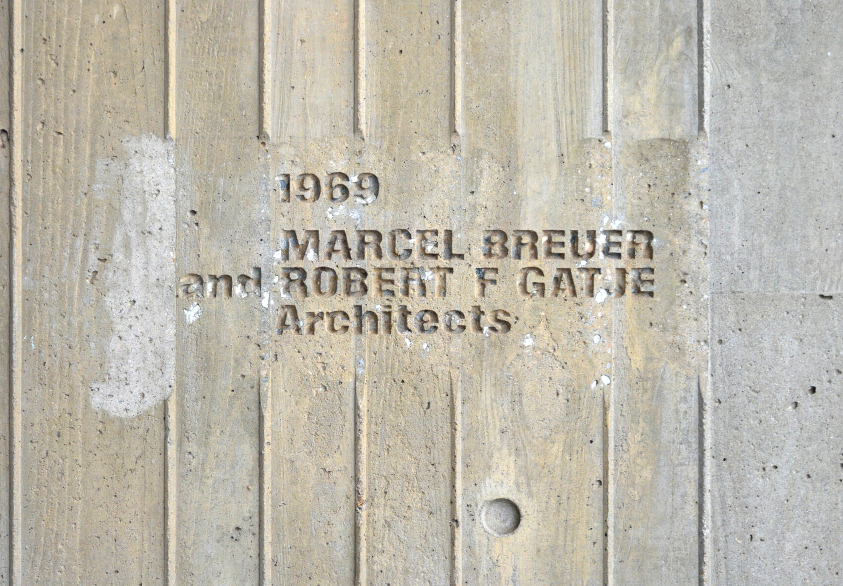 Close-up photograph of a concrete wall panel with an embedded sign that reads: "1968 MARCEL BREUER and ROBERT F. GATJE Architects".