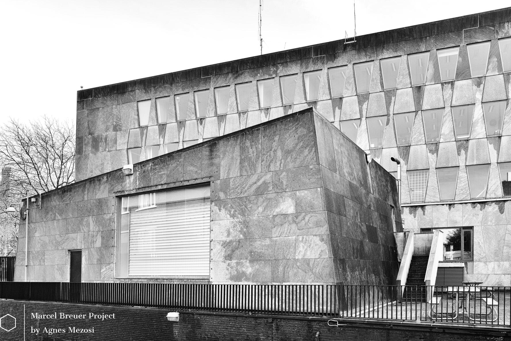 A separate, sculptural concrete annex building in the embassy's courtyard with a unique, angular geometry and a flat roof, standing in contrast to the repetitive windows of the main structure.