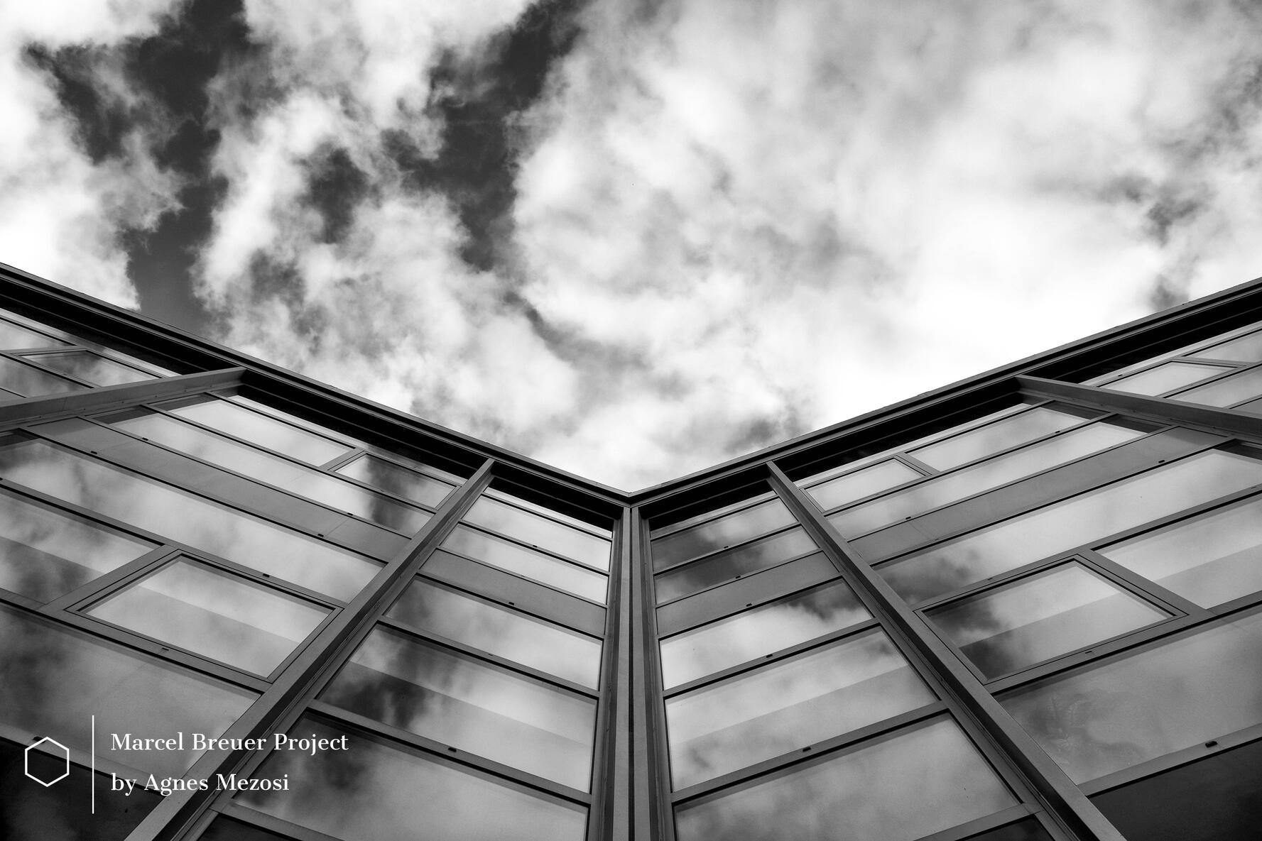 Black and white architectural photograph of the Van Leer building's glass facade reflecting a cloudy sky.