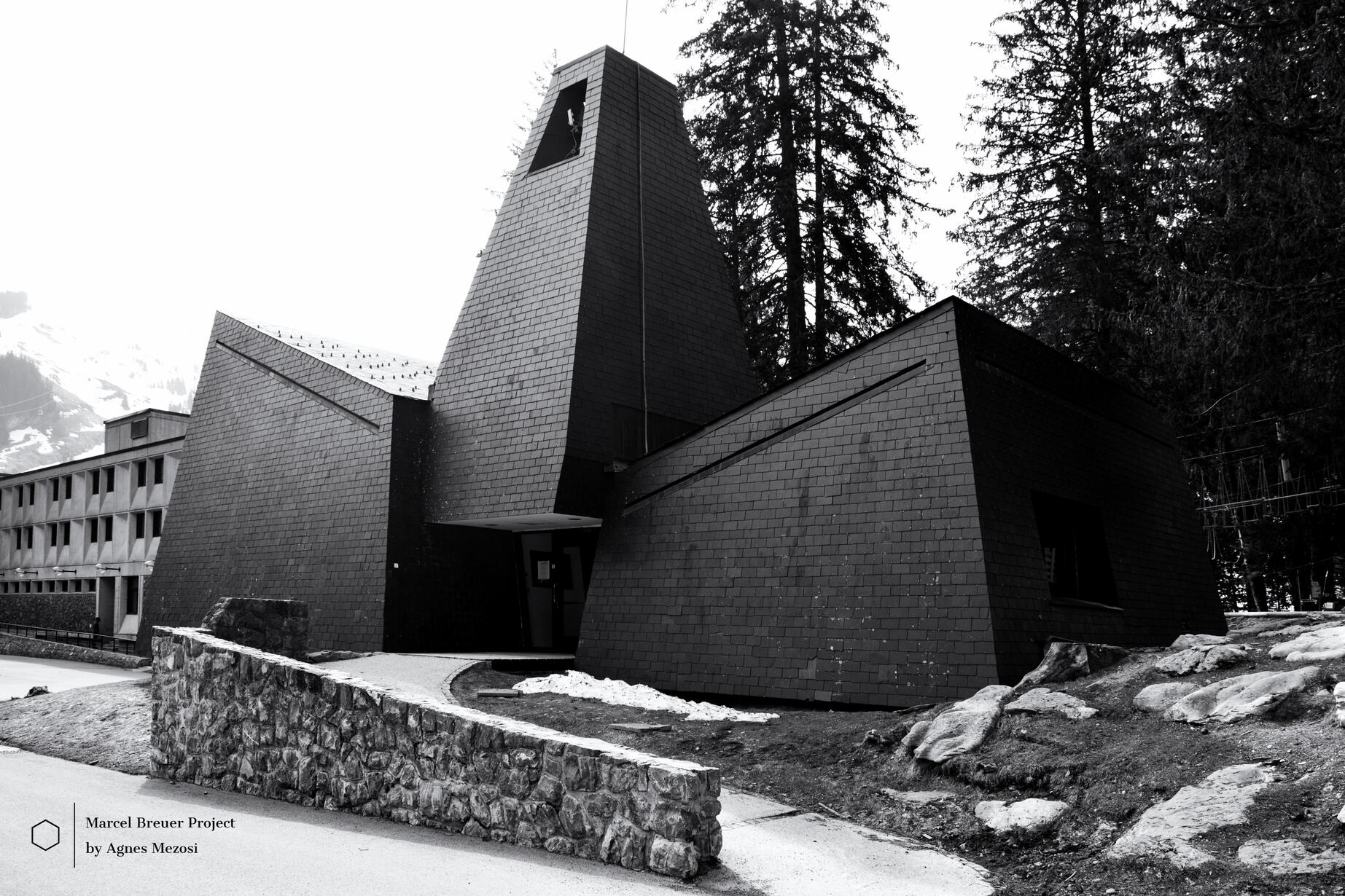 Exterior view of the dark, geometric chapel in Flaine, designed by Marcel Breuer, surrounded by evergreen trees.