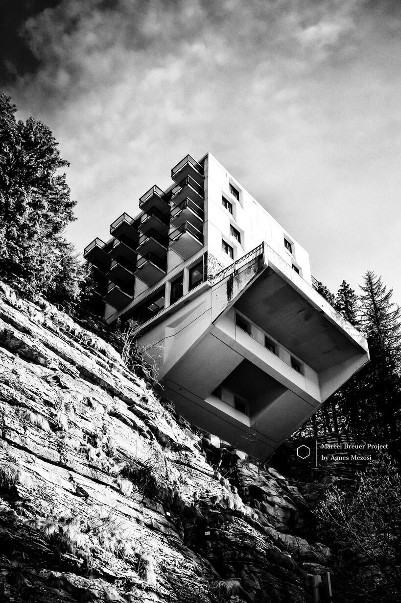 Low-angle black and white shot of a brutalist hotel building in Flaine, dramatically overhanging a steep rocky cliff.